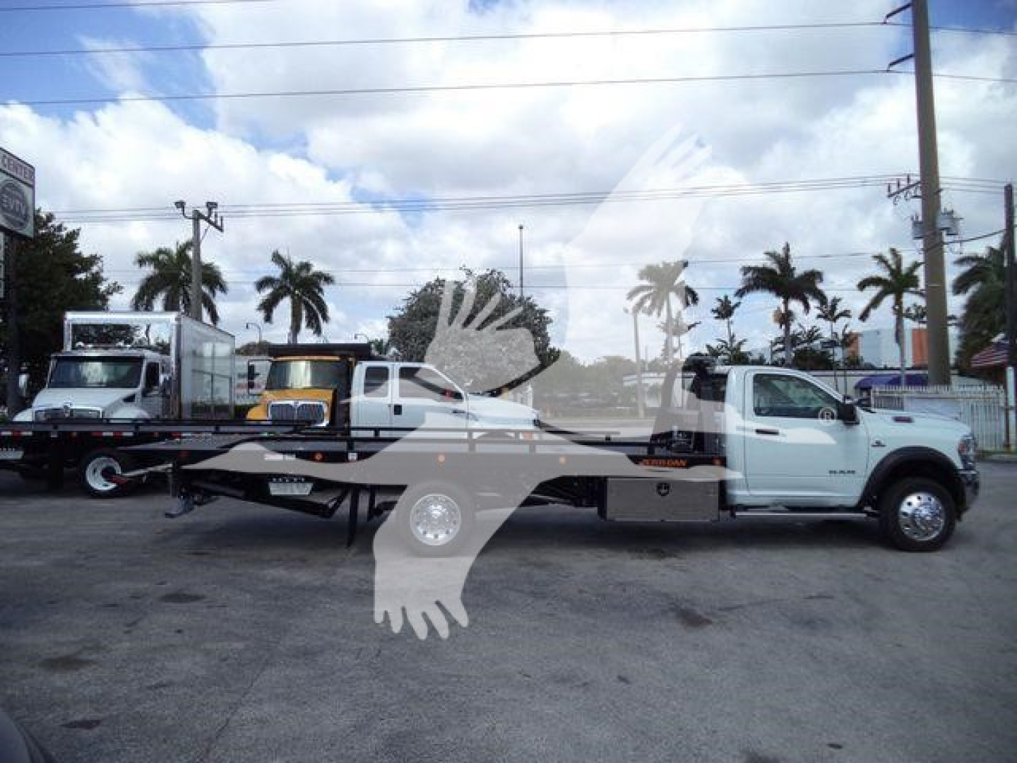 Ram 5500 rollback tow truck side view showing long flatbed with white cab and white tow truck in a dealership lot