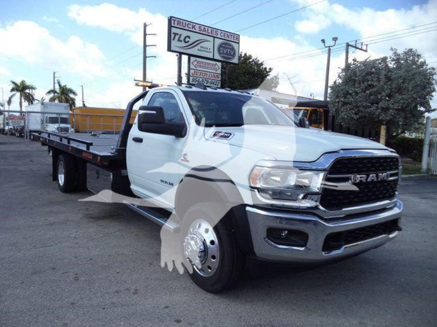 Ram 5500 tow truck with flatbed, front grille RAM badge, white cab, dual rear wheels, dealership lot in background.