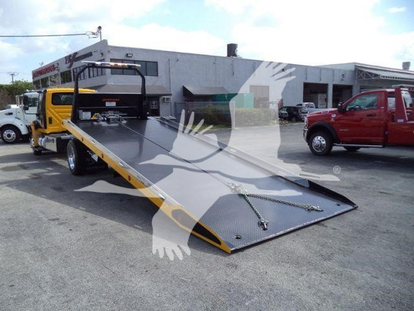 2019 International 4300 rollback truck with a tilted flatbed in a dealership lot showing the equipment and surrounding vehicles.