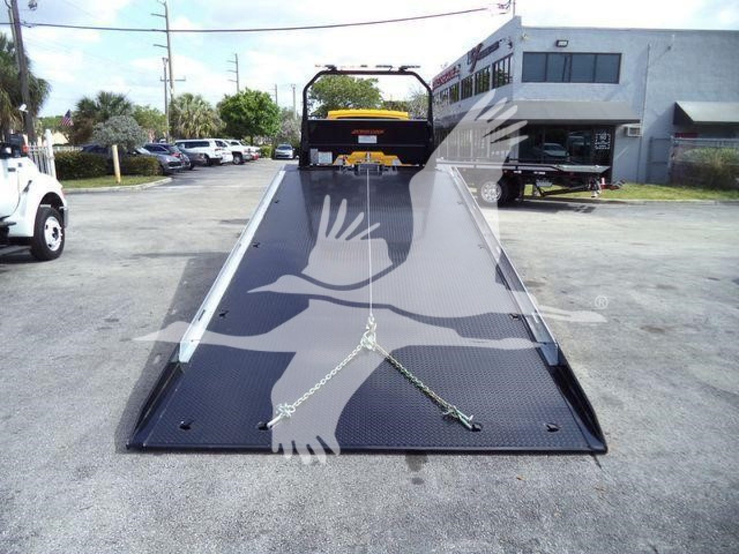 Truck rollback bed with ramp extended, 2019 International 4300 stock image. The scene shows a ramped flatbed in a parking lot with a building in background.