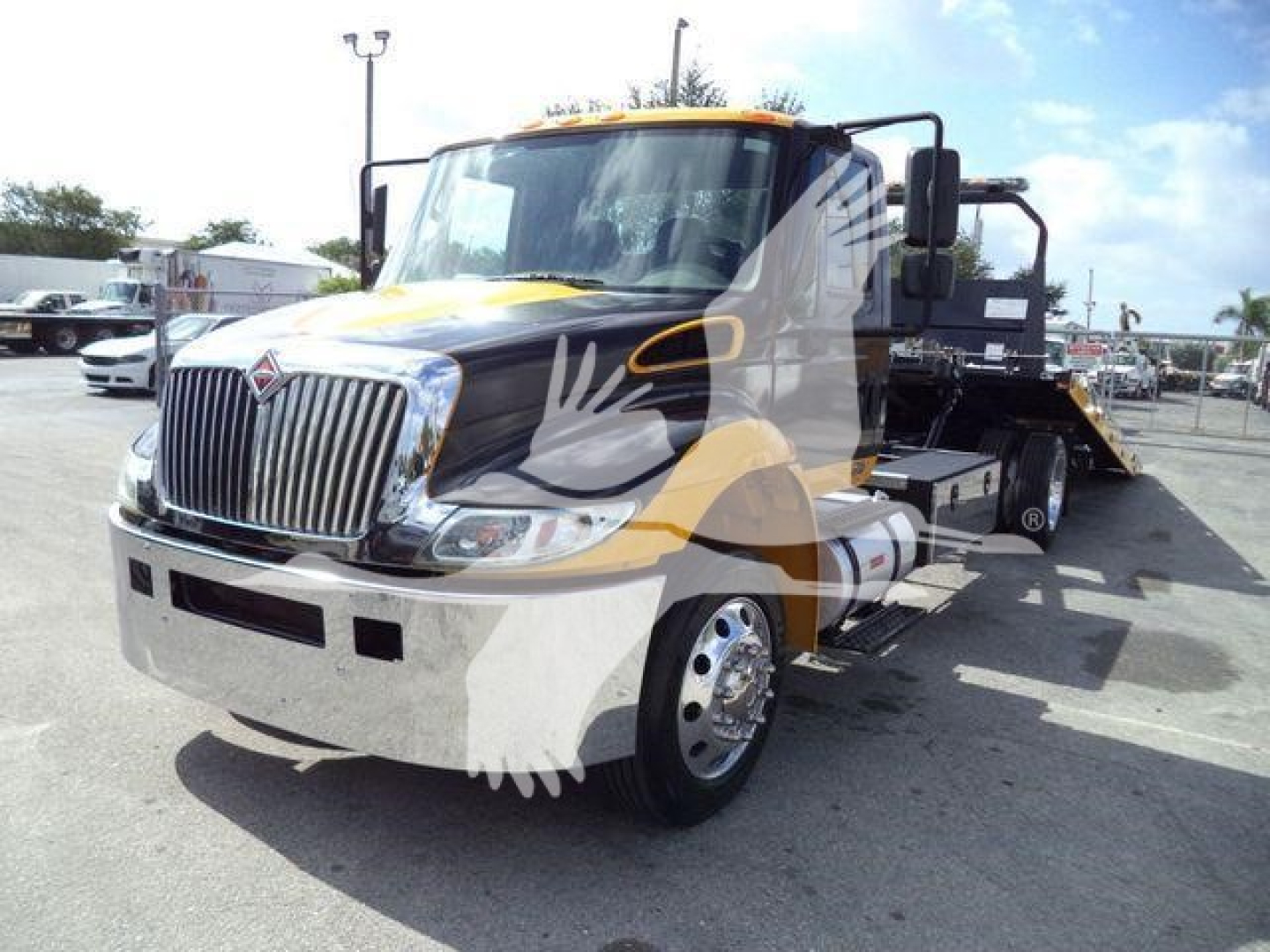 Tow truck medium-duty International 4300 rollback with a black and yellow color scheme and chrome grille.