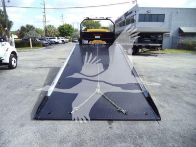 Truck rollback bed with ramp extended, 2019 International 4300 stock image. The scene shows a ramped flatbed in a parking lot with a building in background.