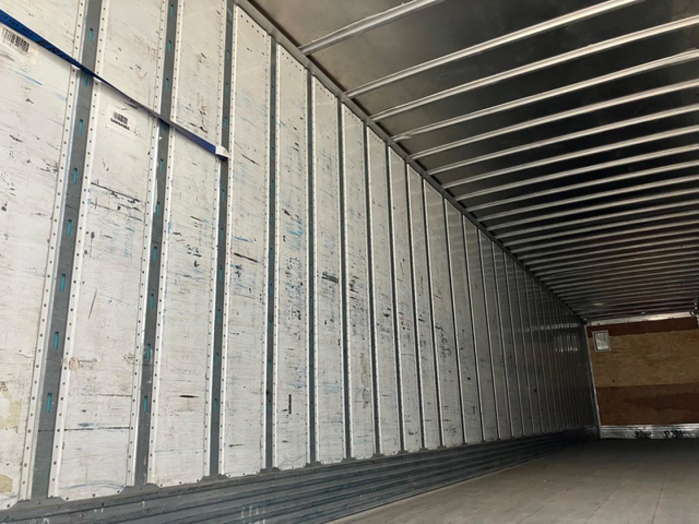 Van trailer interior showing metal side walls with vertical supports and a dark rear end.