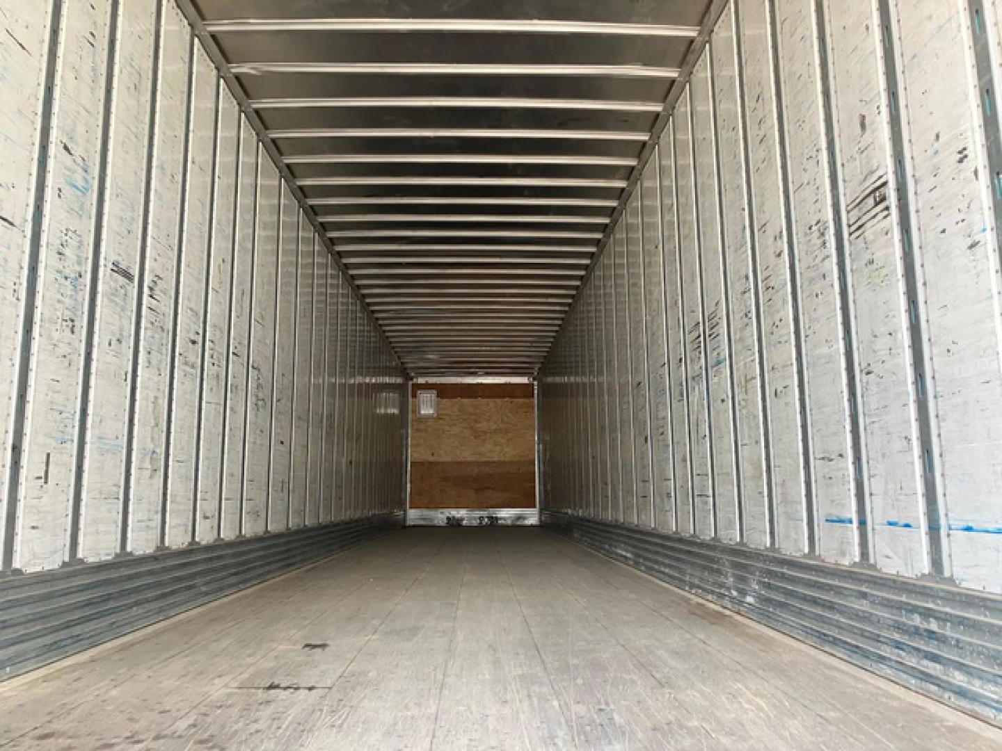 Trailer interior: empty rectangular cargo space with aluminum sidewalls and ribbed ceiling, plywood bulkhead at rear, wooden floor marks.