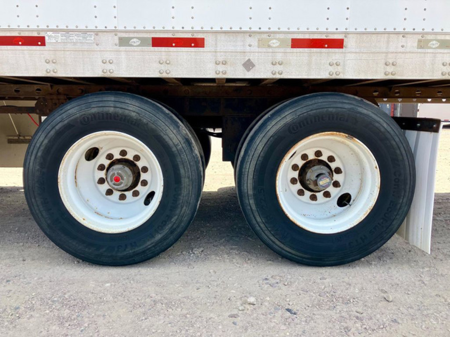 Dual trailer wheels showing tires and white steel rims under a trailer with reflected light.