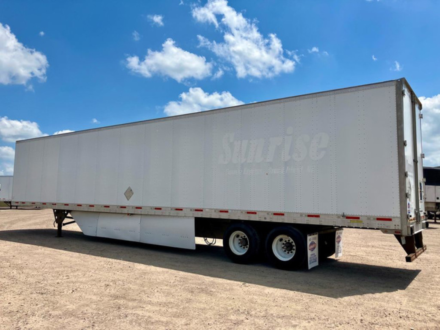 Utility van trailer showing Sunrise logo on side and triple axle with landing gear, white semi-trailer in open lot.