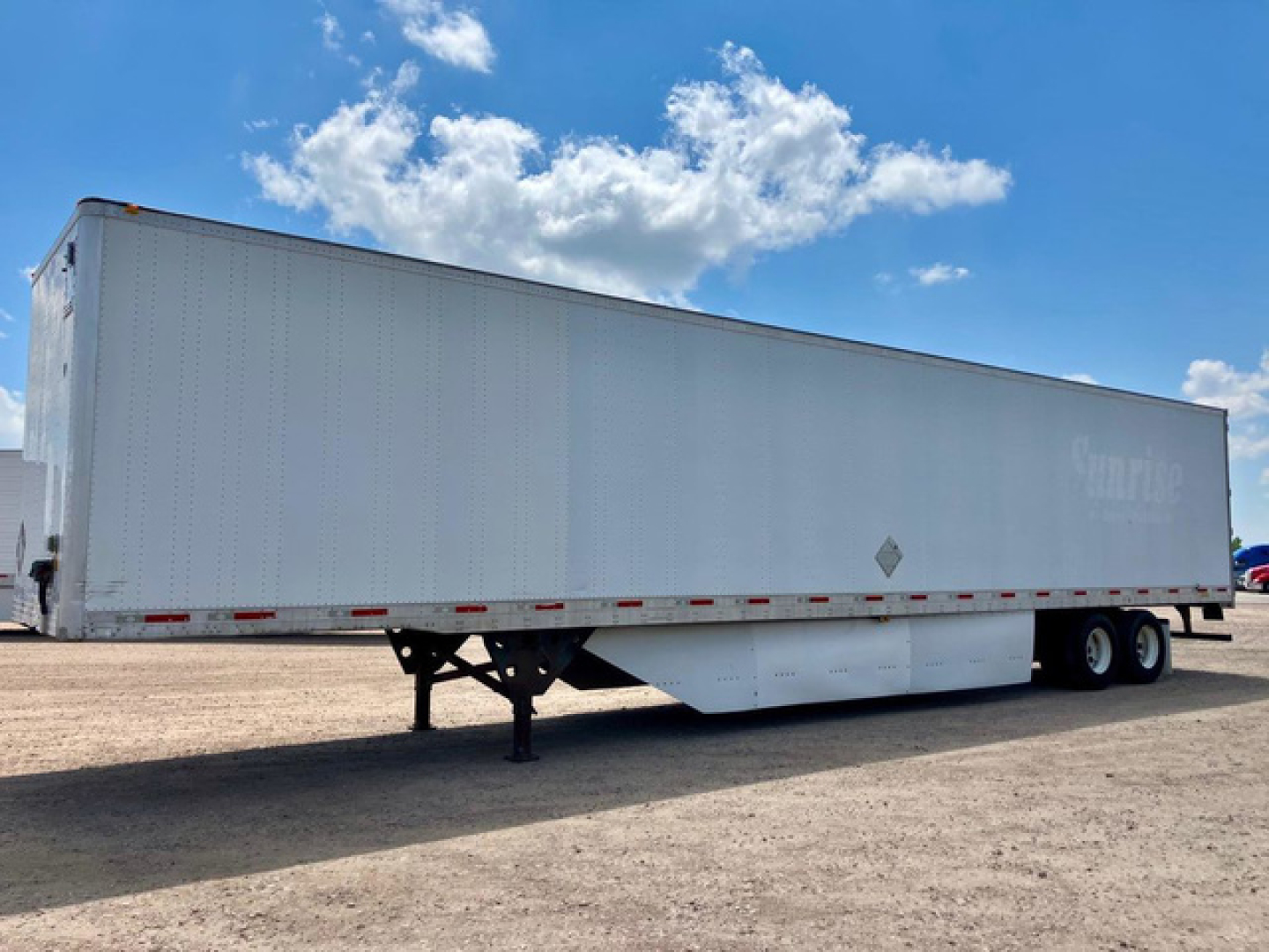 Utility van trailer showing side text and wheel assembly with dual rear axles.