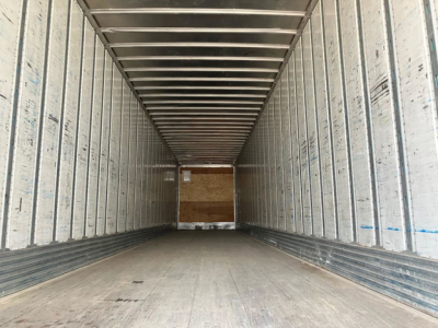 Trailer interior: empty rectangular cargo space with aluminum sidewalls and ribbed ceiling, plywood bulkhead at rear, wooden floor marks.