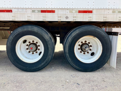 Dual trailer wheels showing tires and white steel rims under a trailer with reflected light.