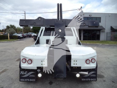 Tow truck rear view with heavy-duty winch apparatus mounted on truck bed, twin vertical guide posts, white body, and taillights visible.