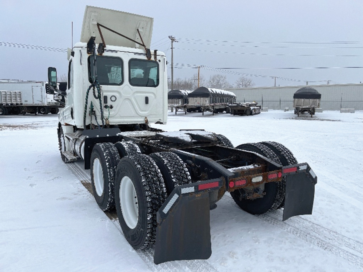 Truck chassis view showing rear dual-axle configuration with mud flaps and snow-covered ground.