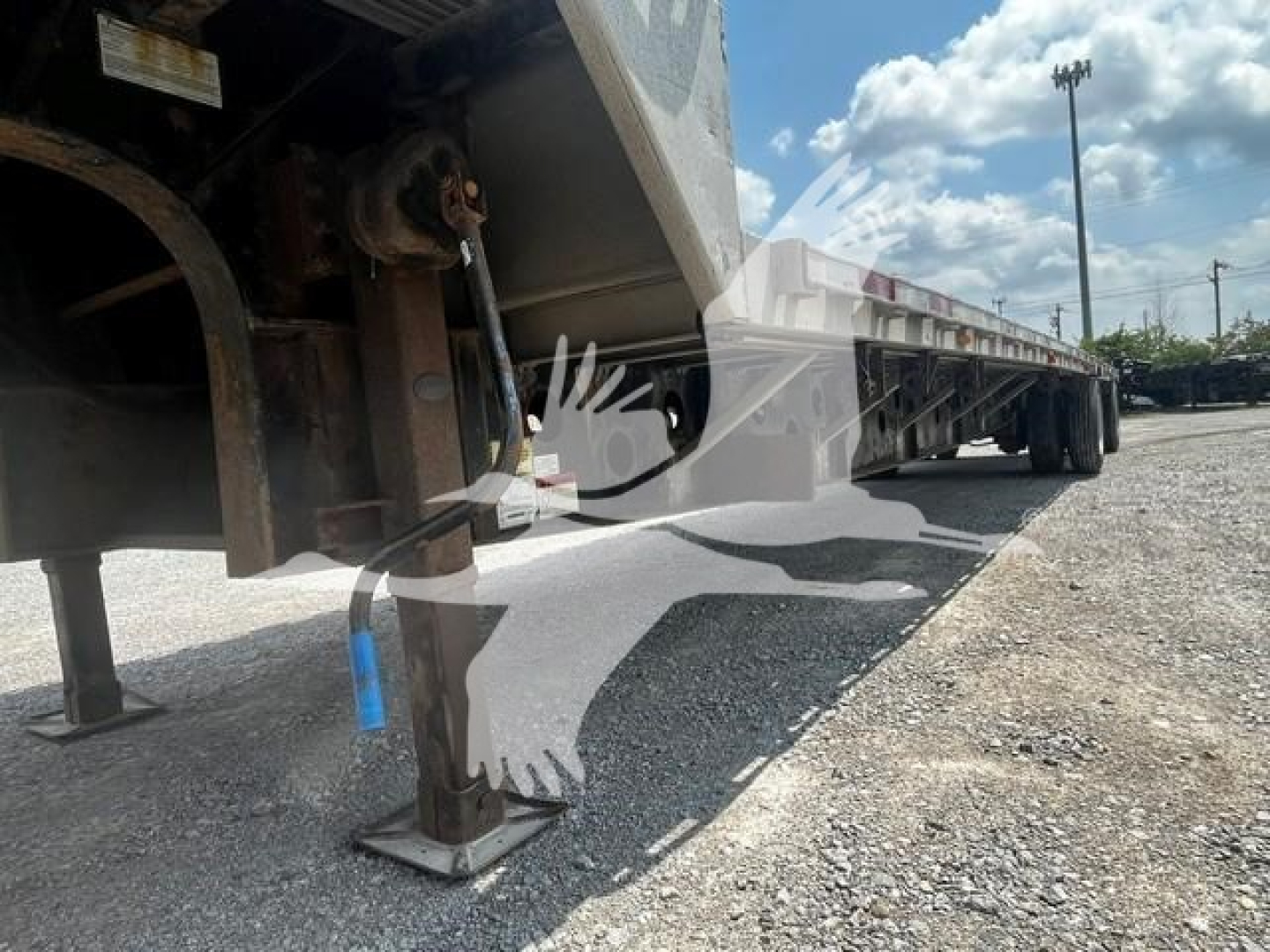 Transcraft DTL-2000 trailer showing stabilizer jacks and undercarriage with blue stake, side deck and gravel ground.
