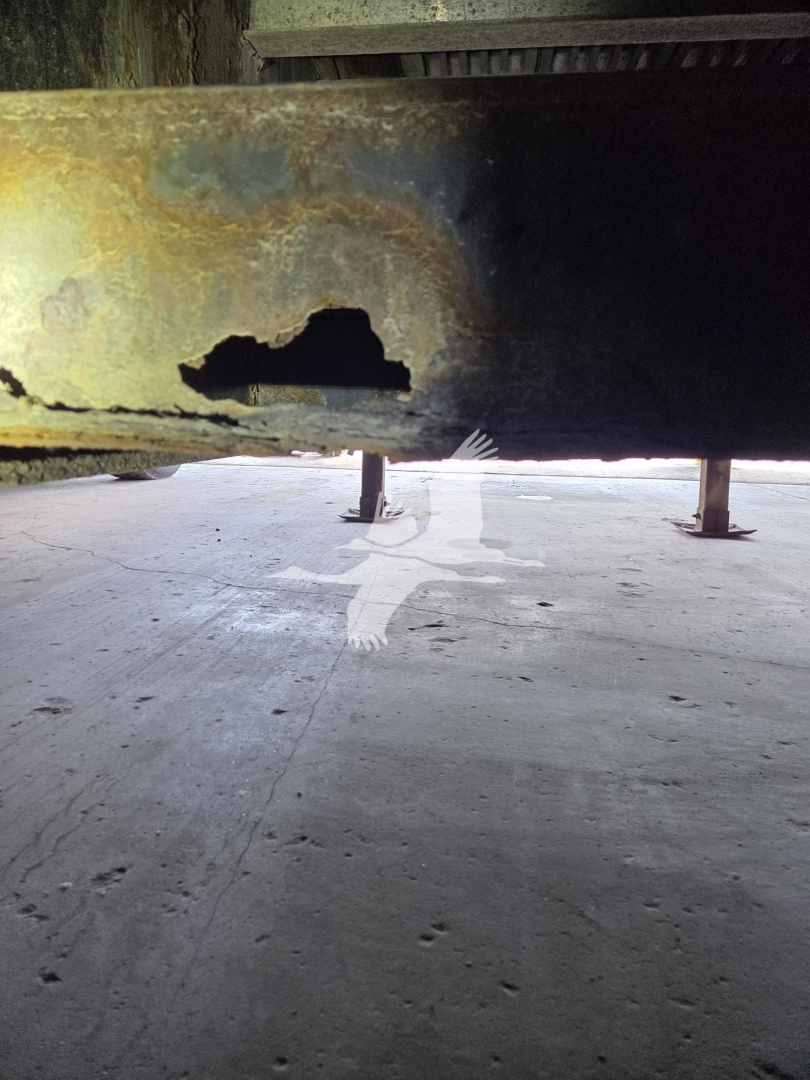 Trailer frame underside showing a large hole in the metal crossmember with rust and support legs visible.