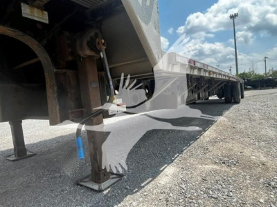Transcraft DTL-2000 trailer showing stabilizer jacks and undercarriage with blue stake, side deck and gravel ground.