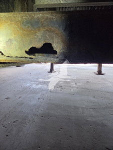 Trailer frame underside showing a large hole in the metal crossmember with rust and support legs visible.