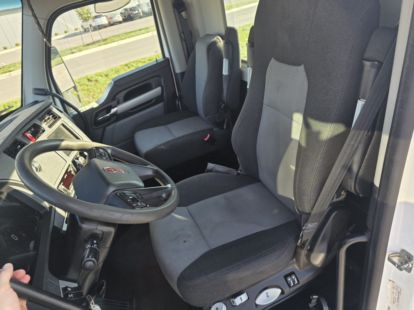 Truck cab interior showing steering wheel and two seats in a Kenworth T680, dashboard and gear selector visible.