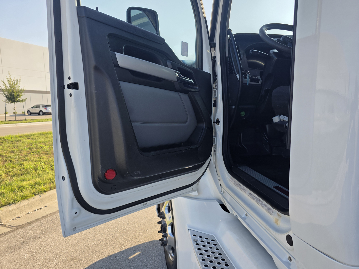 Kenworth T680 truck door open showing interior cabin with black and gray door panel, steps, and part of dashboard.