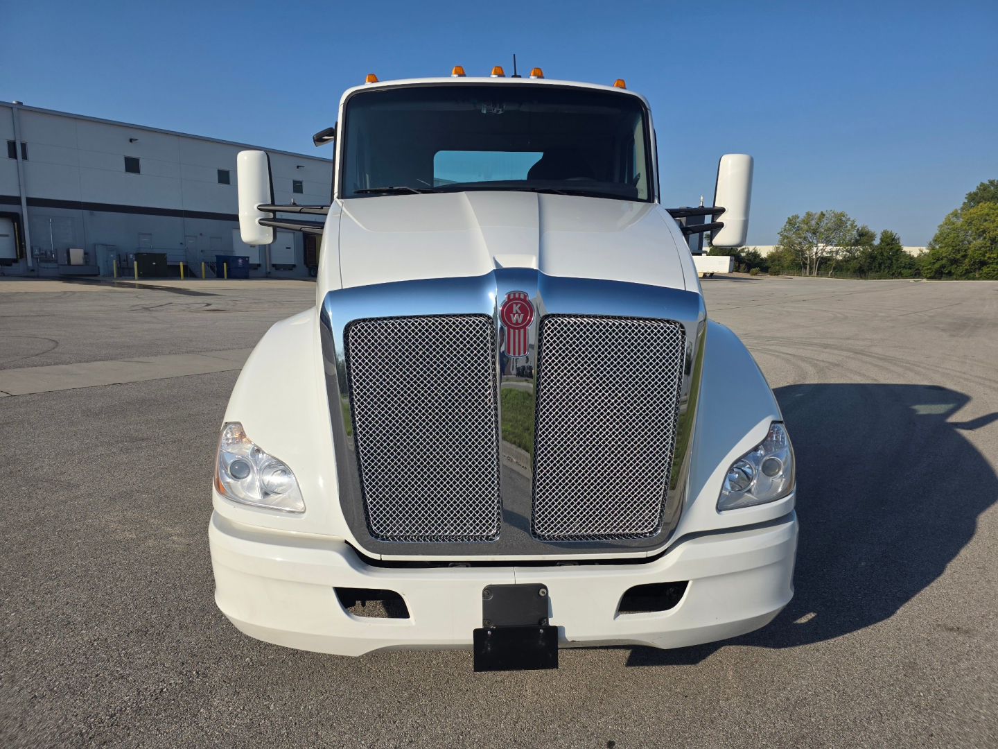 Kenworth T680 front view showing large mesh grille, dual headlights, white cab, side mirrors, and bumper.