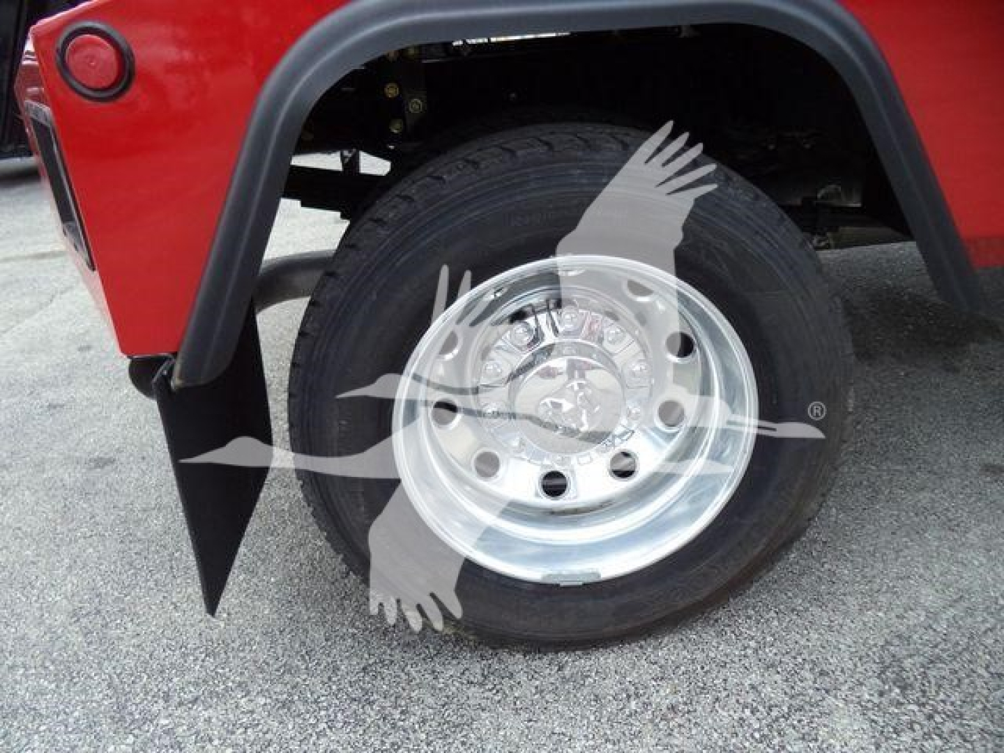 Truck wheel and tire visible with fender flare and winch category vehicle, chrome wheel, tire tread, red body panel in background.
