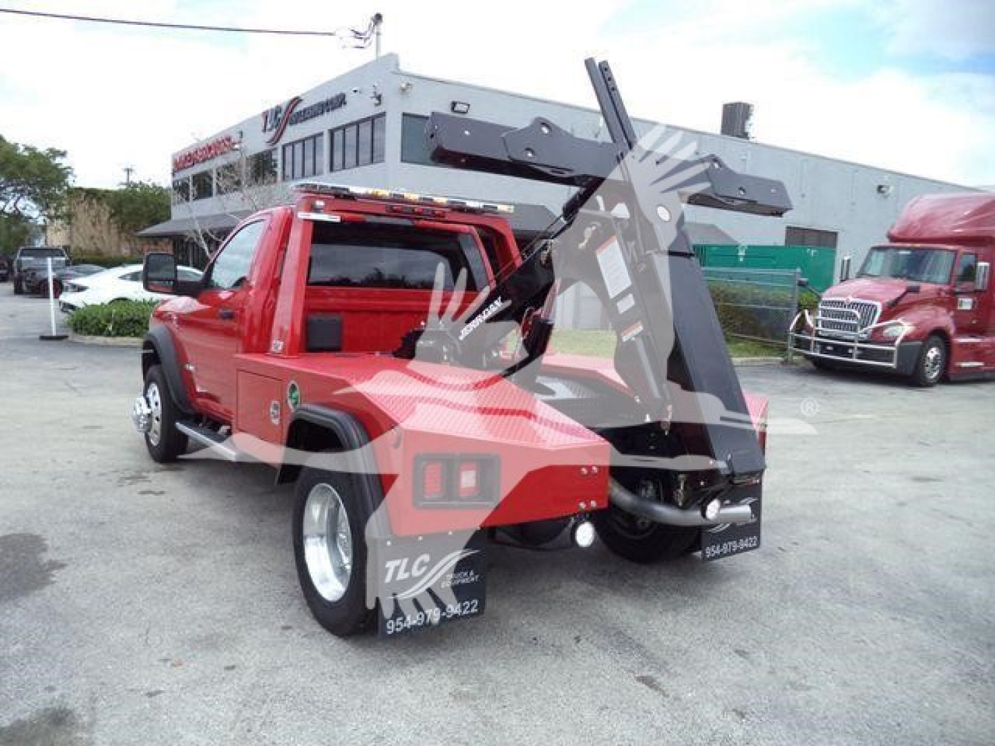 Red Ram 4500 tow truck with front mounted winch in yard, lift crane folded back, rear dual wheels visible, dealership building in background.