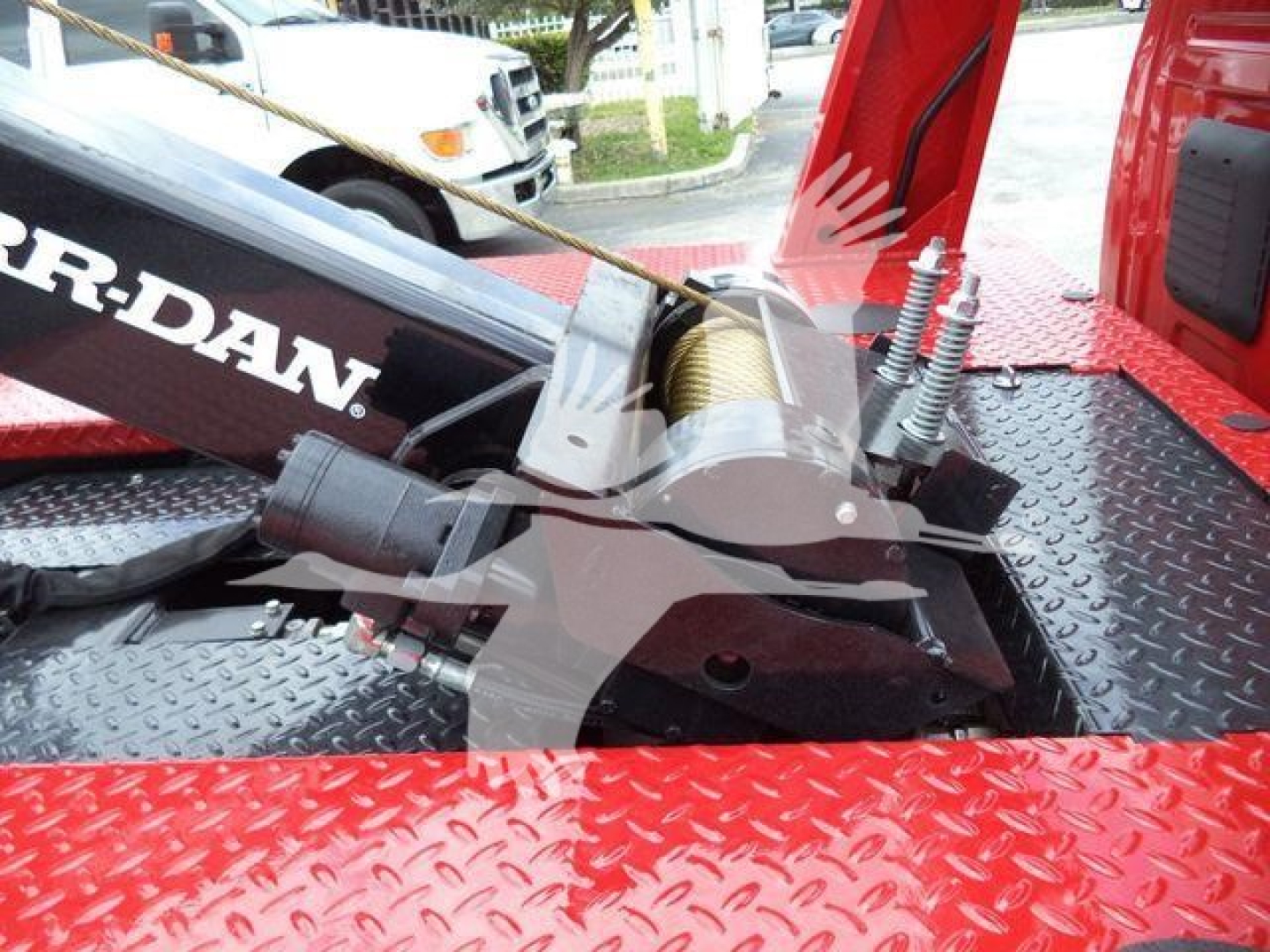 Winch motor and cable assembly installed on a red utility truck bed with diamond plate surface showing the brand name 'WARN-DAN' partially visible.