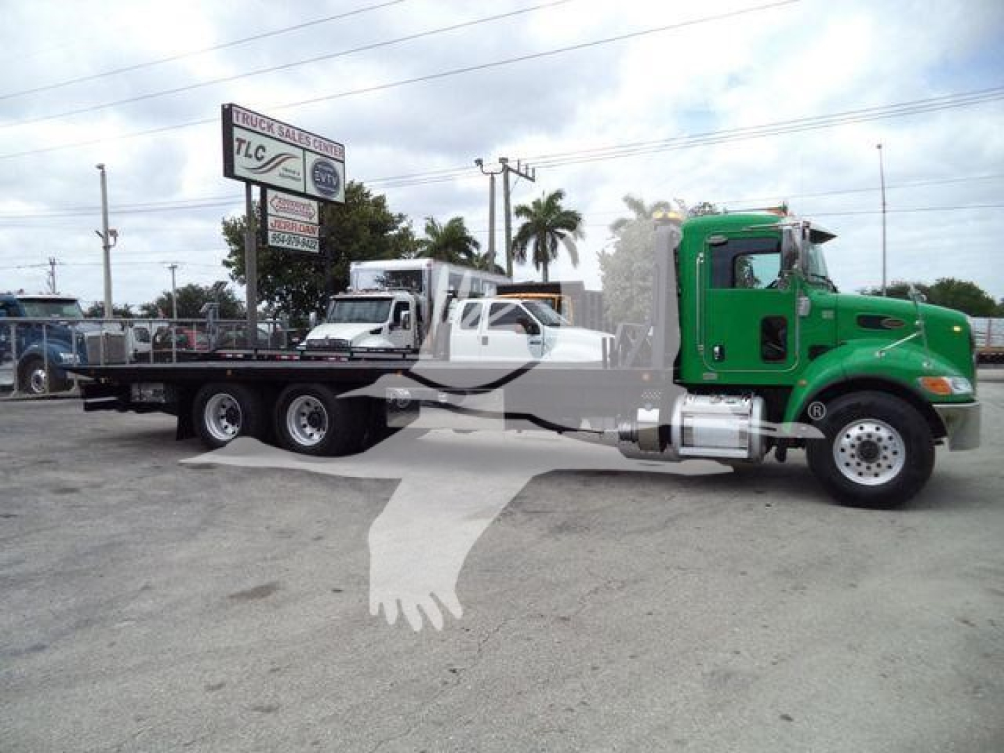 Peterbilt 348 rollback truck with a green cab and long flatbed trailer, stock number T40939FM visible on a sign in the background.