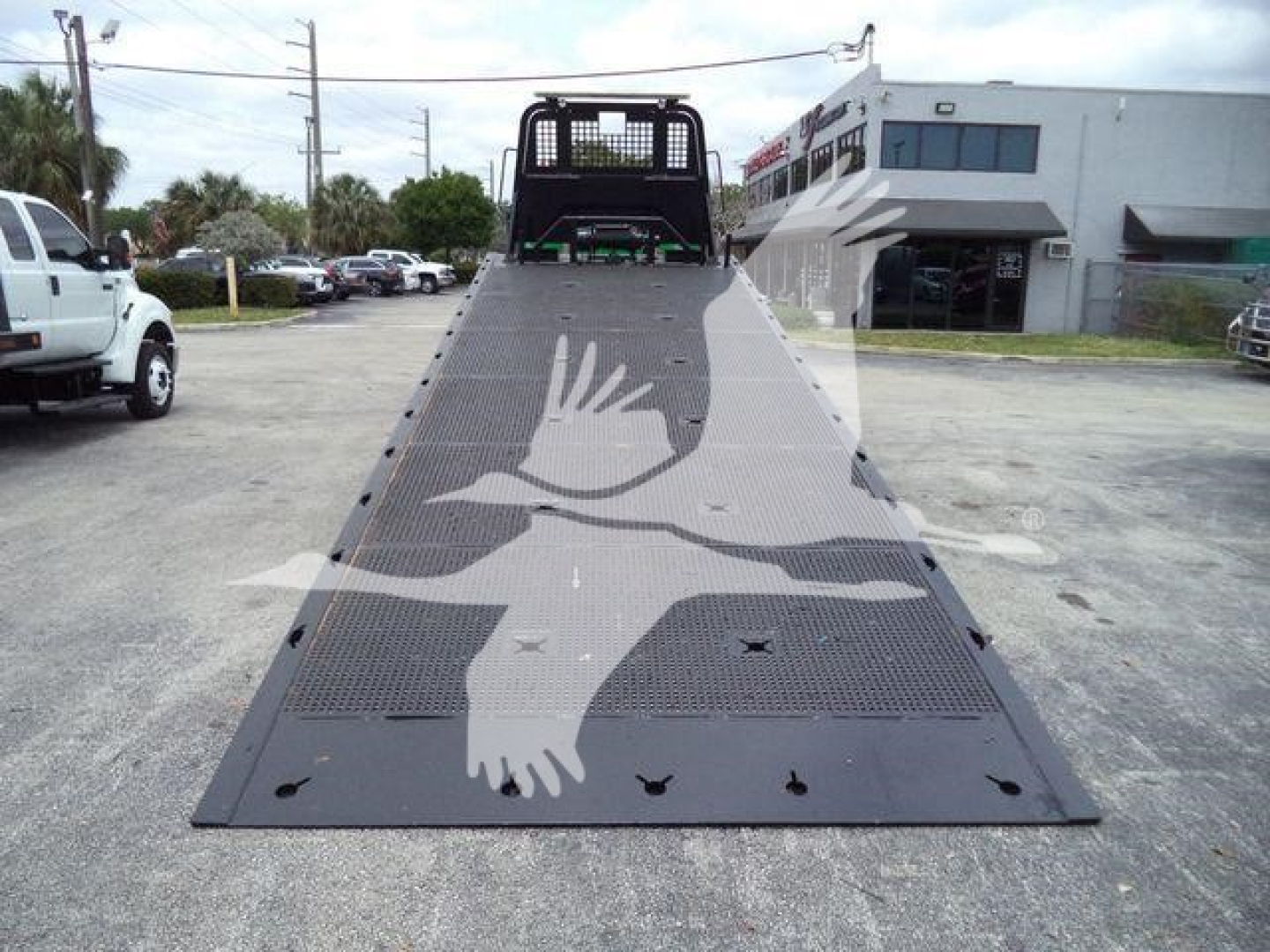 2016 Peterbilt 348 rollback truck with long flatbed ramp, loading platform, and rear cab cage visible in a dealership lot.