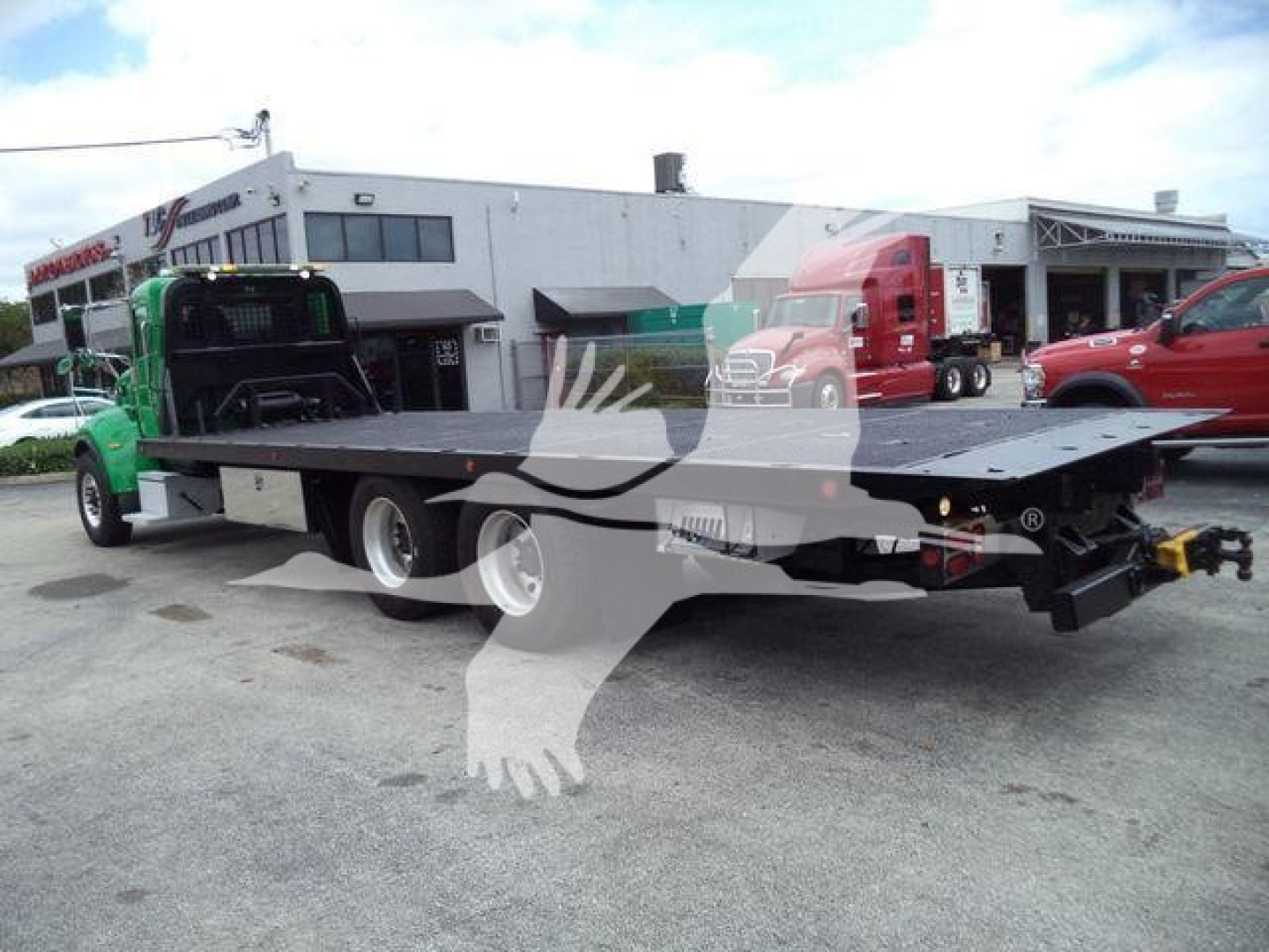 Peterbilt 348 rollback tow truck with a flatbed, side view showing the long carrier bed and green cab, warehouse background.