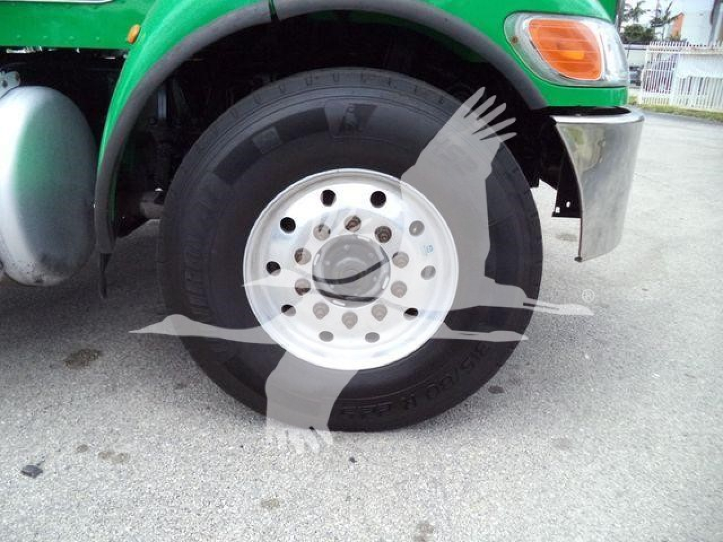 Peterbilt truck front wheel and fender with green cab, chrome bumper, and visible wheel hub, tire sidewall and rim.