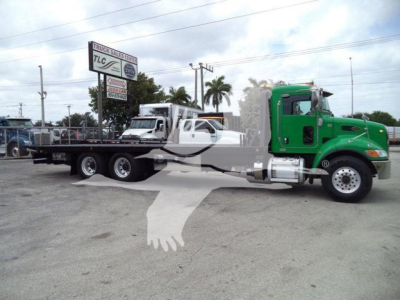 Peterbilt 348 rollback truck with a green cab and long flatbed trailer, stock number T40939FM visible on a sign in the background.
