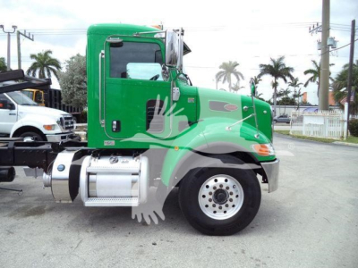 Green Peterbilt 348 truck in side view with black fender, chrome fuel tanks, and round wheel; visible decals and a white storage area in background.