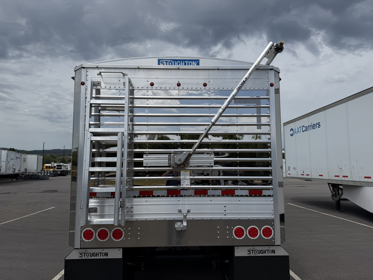 Rear view of a 2027 Stoughton aluminum grain hopper trailer with 68" corrugated sidewalls and rear ladder, braced with a diagonal support.