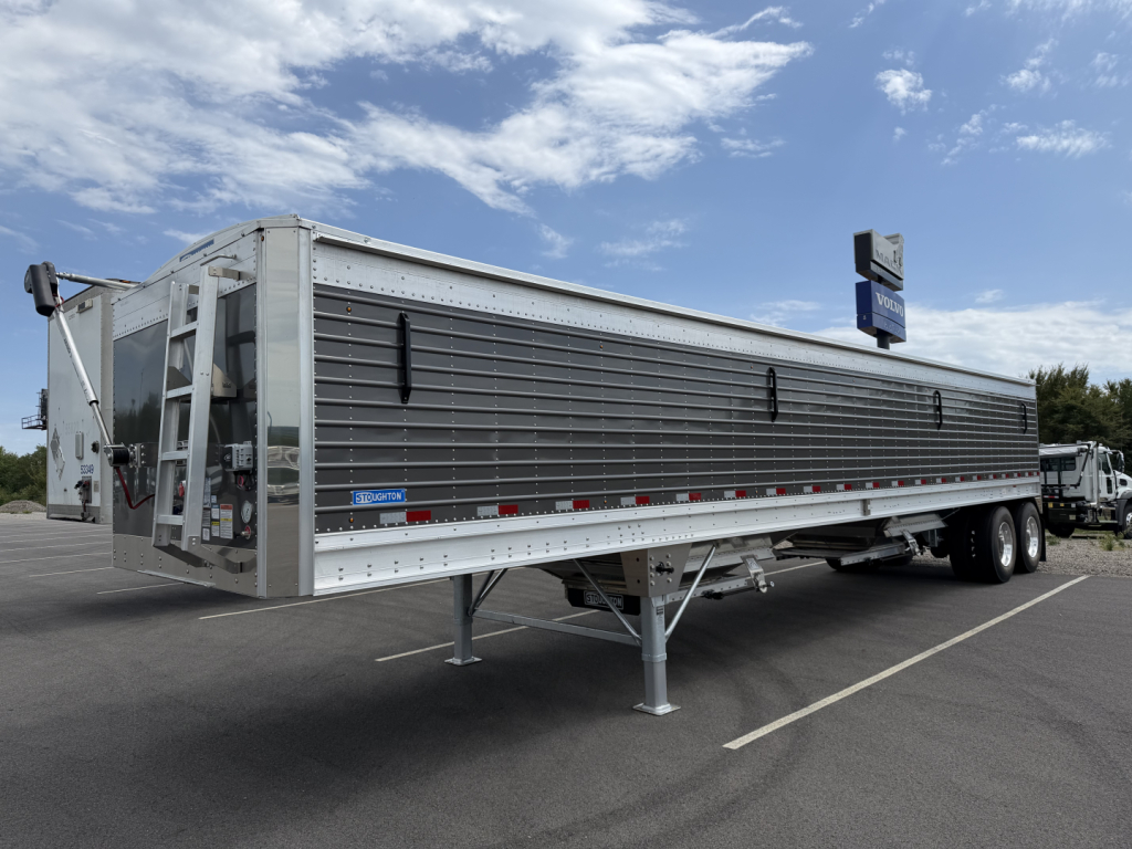 Stoughton 40' aluminum grain hopper trailer with 68-inch corrugated sidewalls, triple-axle configuration, loading chute and ladder visible, side decals and reflective tape along bottom edge.