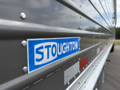 Stoughton brand trailer side panel showing blue Stoughton logo plate with riveted metal siding and reflective striping.