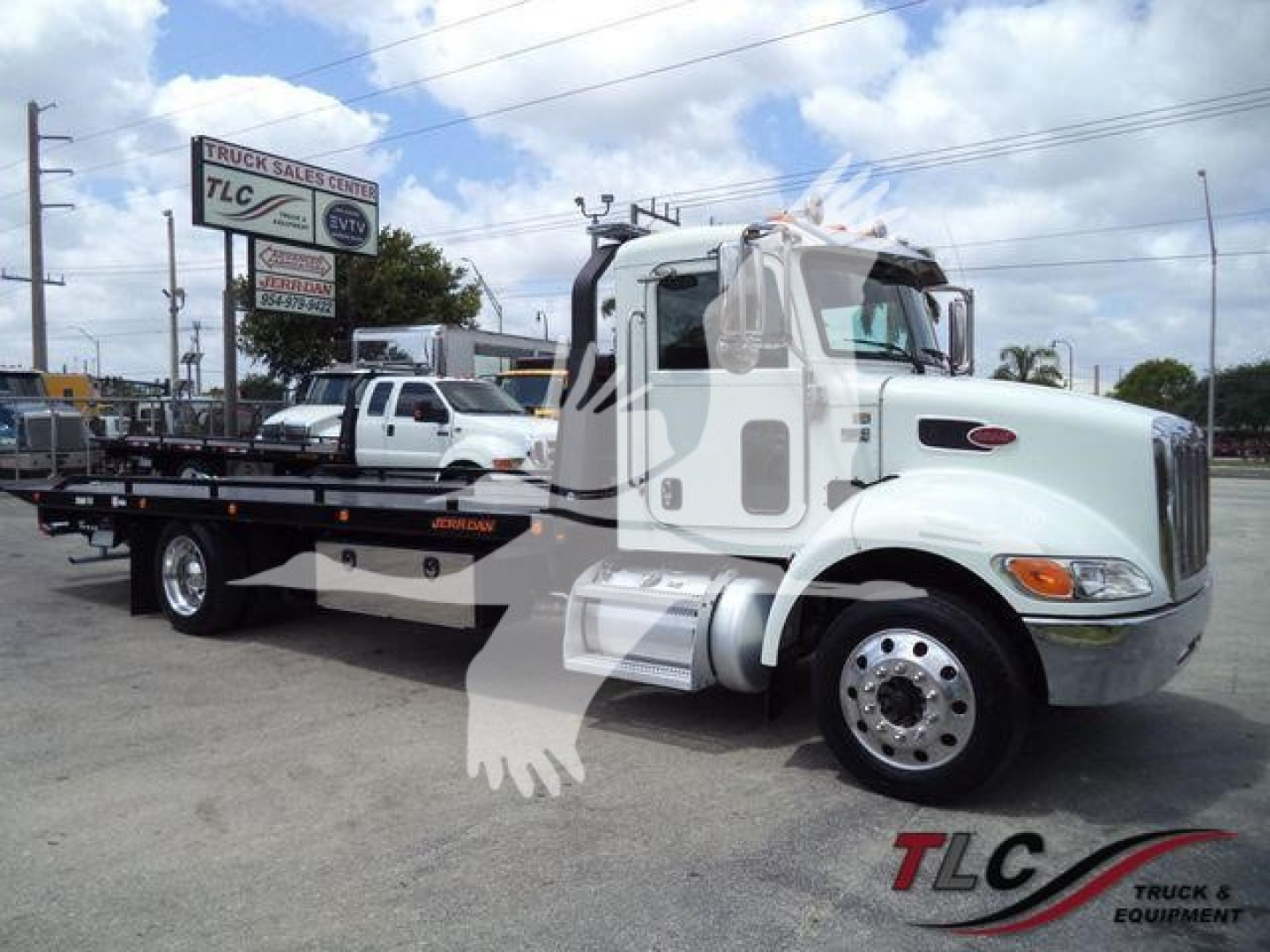 Peterbilt 337 rollback w/ flatbed showing cab and wheel, truck in dealership lot.