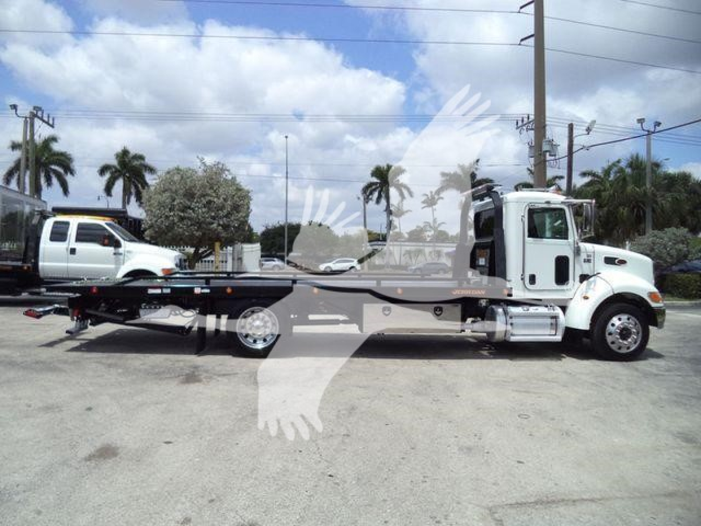 2018 Peterbilt 337 rollback with flatbed chassis, side view showing cab and long wheelbase, truck in a lot with palm trees.