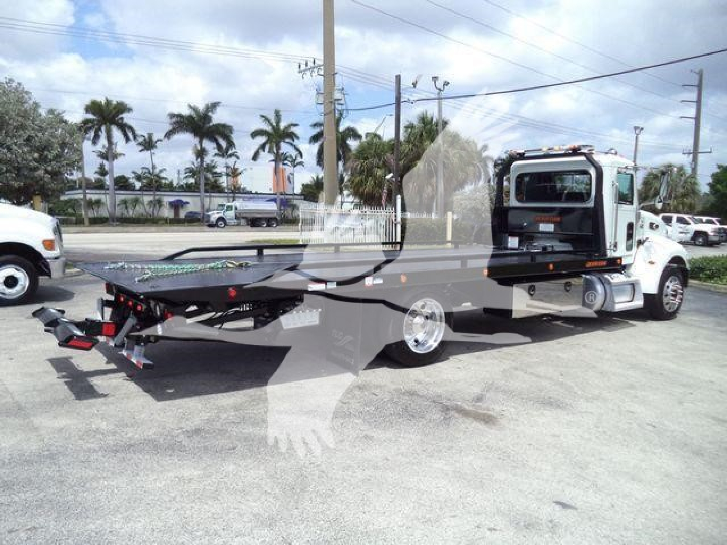 Peterbilt 337 rollback tow truck with flatbed, white cab and black flatbed, side view showing wheel and hydraulic mechanism.
