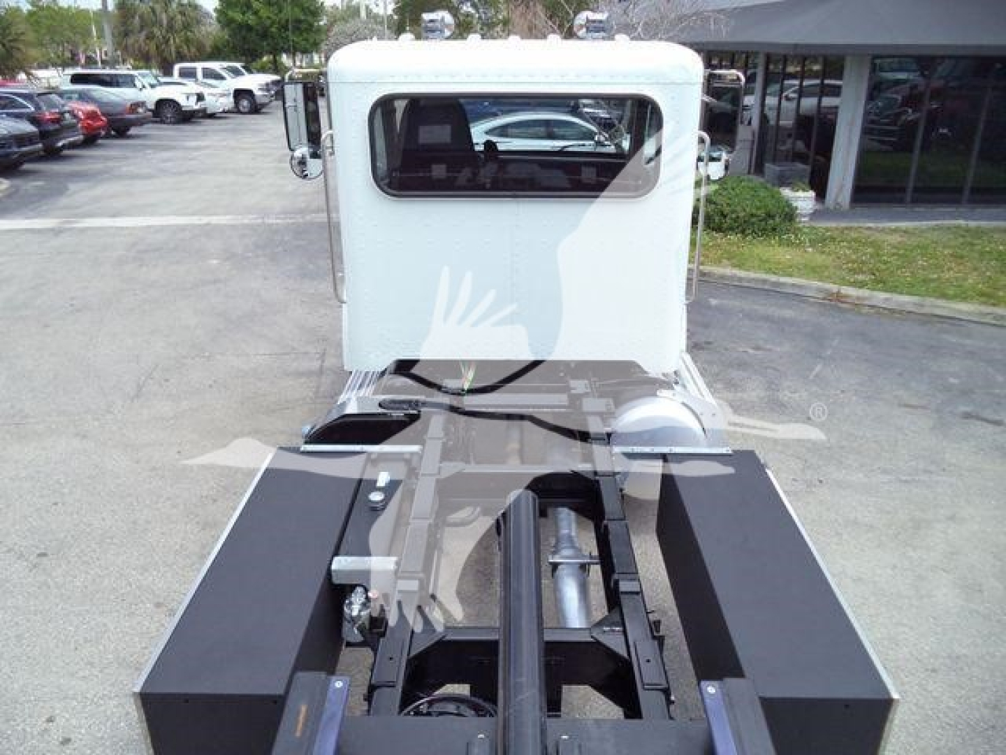 Truck cab and chassis of a 2018 Peterbilt 337 with rollback setup; rear view shows flatbed/rollback area and fifth wheel mounting, light gray cab, black equipment boxes.