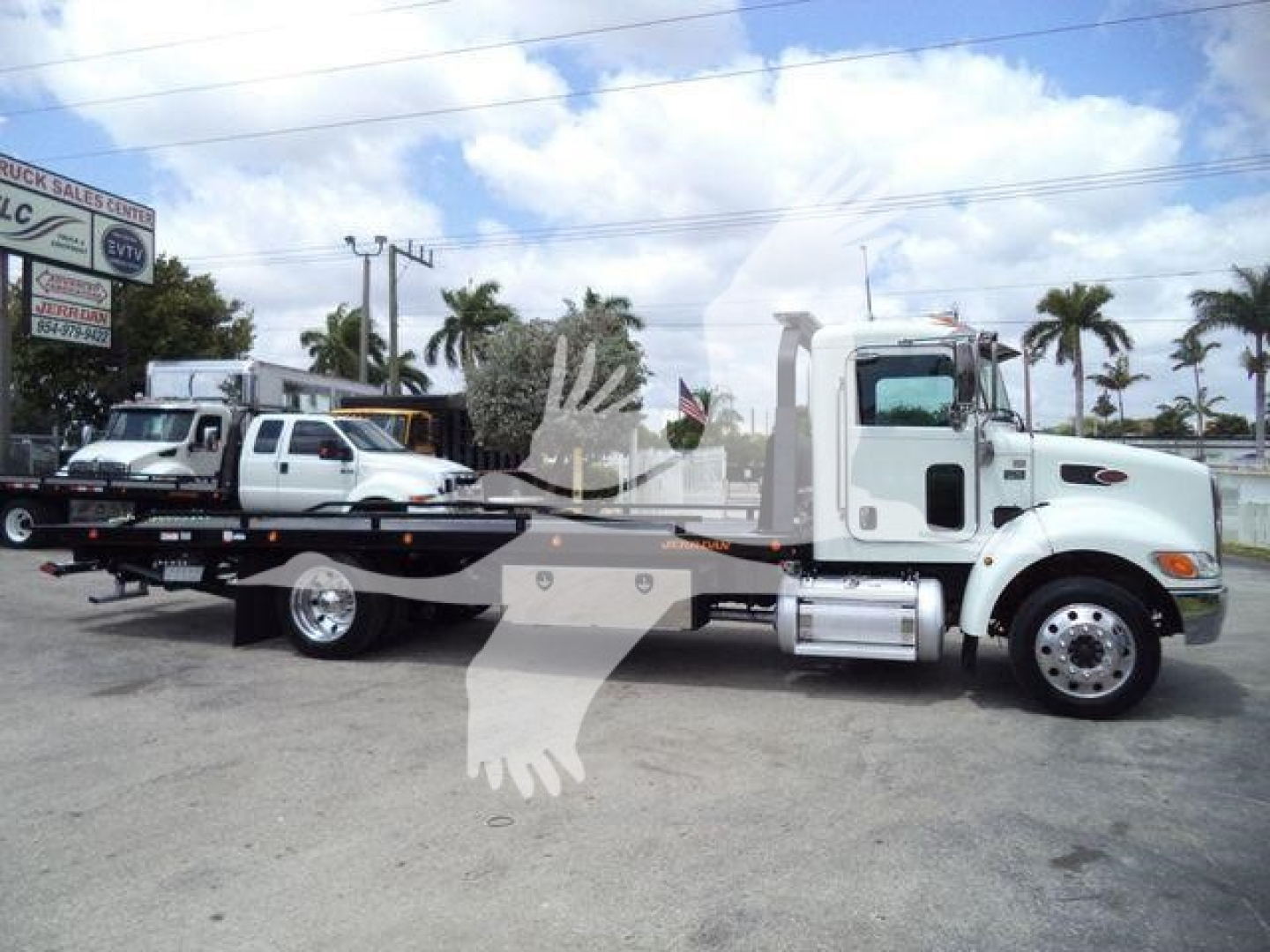 Peterbilt 337 rollback truck side view showing a white cab and a long flatbed trailer.