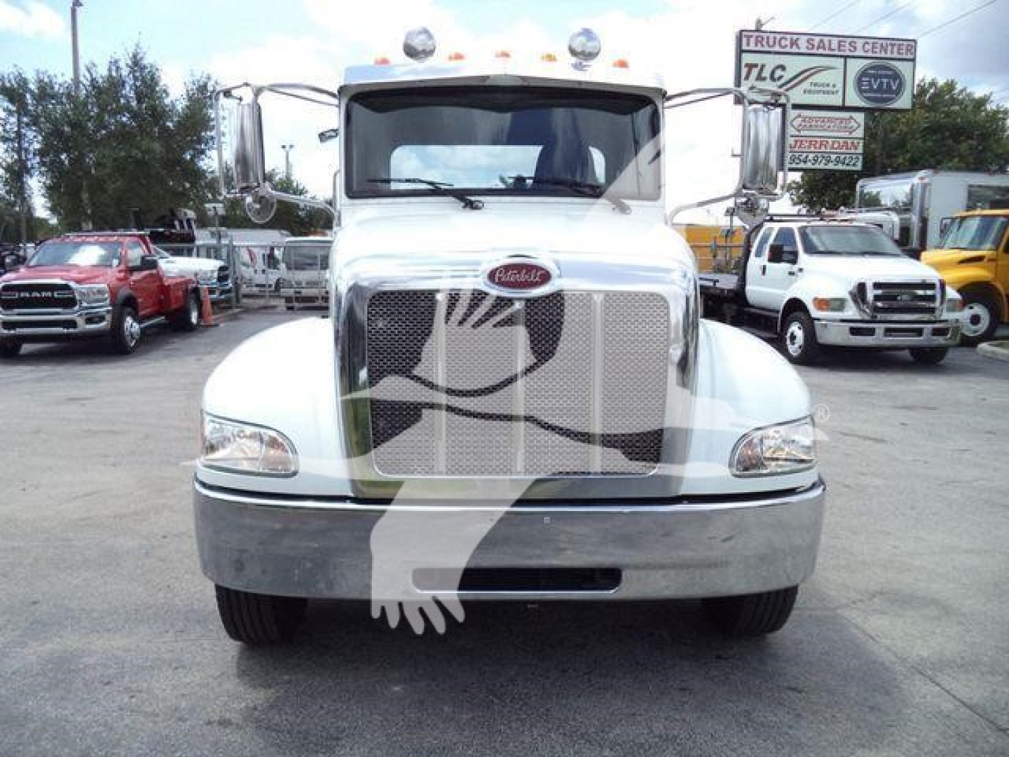 Front view of a white Peterbilt 337 truck in a dealership lot. Grill with Peterbilt emblem, bumper, headlights, and other trucks in background.