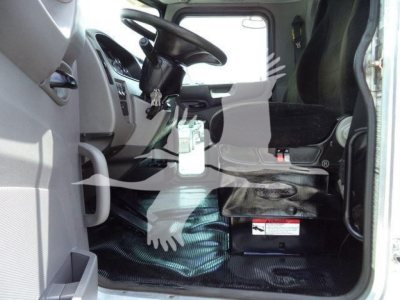 Truck cab interior of a 2018 Peterbilt 337 with steering wheel, driver seat, dashboard, and a large battery or module on the floor; some text labels visible on the panel.