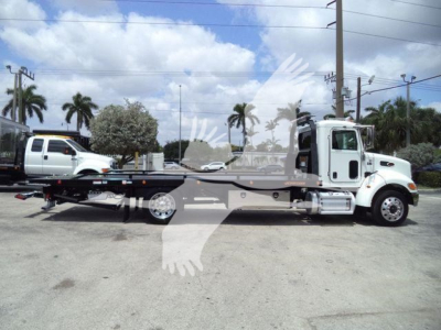 2018 Peterbilt 337 rollback with flatbed chassis, side view showing cab and long wheelbase, truck in a lot with palm trees.