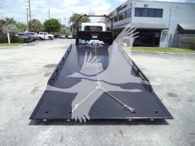 Flatbed rollback truck bed of a 2018 Peterbilt 337 with a black diamond-plate surface, viewed from front, securing chains and winch point.