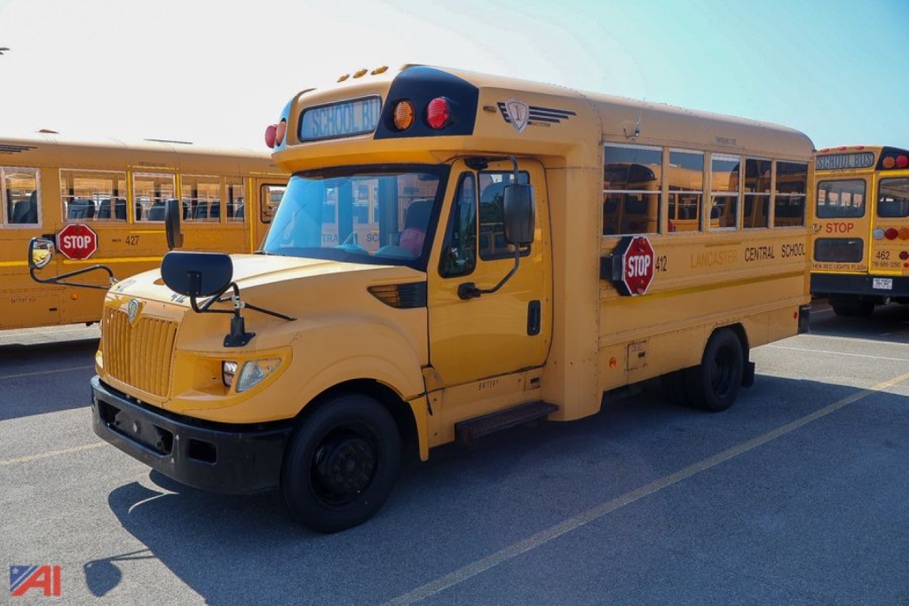 School bus with stop sign extended showing AE Series mid-size bus; text 'SCHOOL BUS' on hood and side, yellow exterior, front grille, dual mirrors, roof emergency lights.