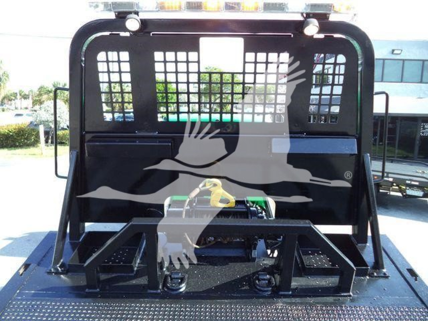Loader attachment on Freightliner M2 106 rollback truck bed with hydraulic hookup and protective cage.