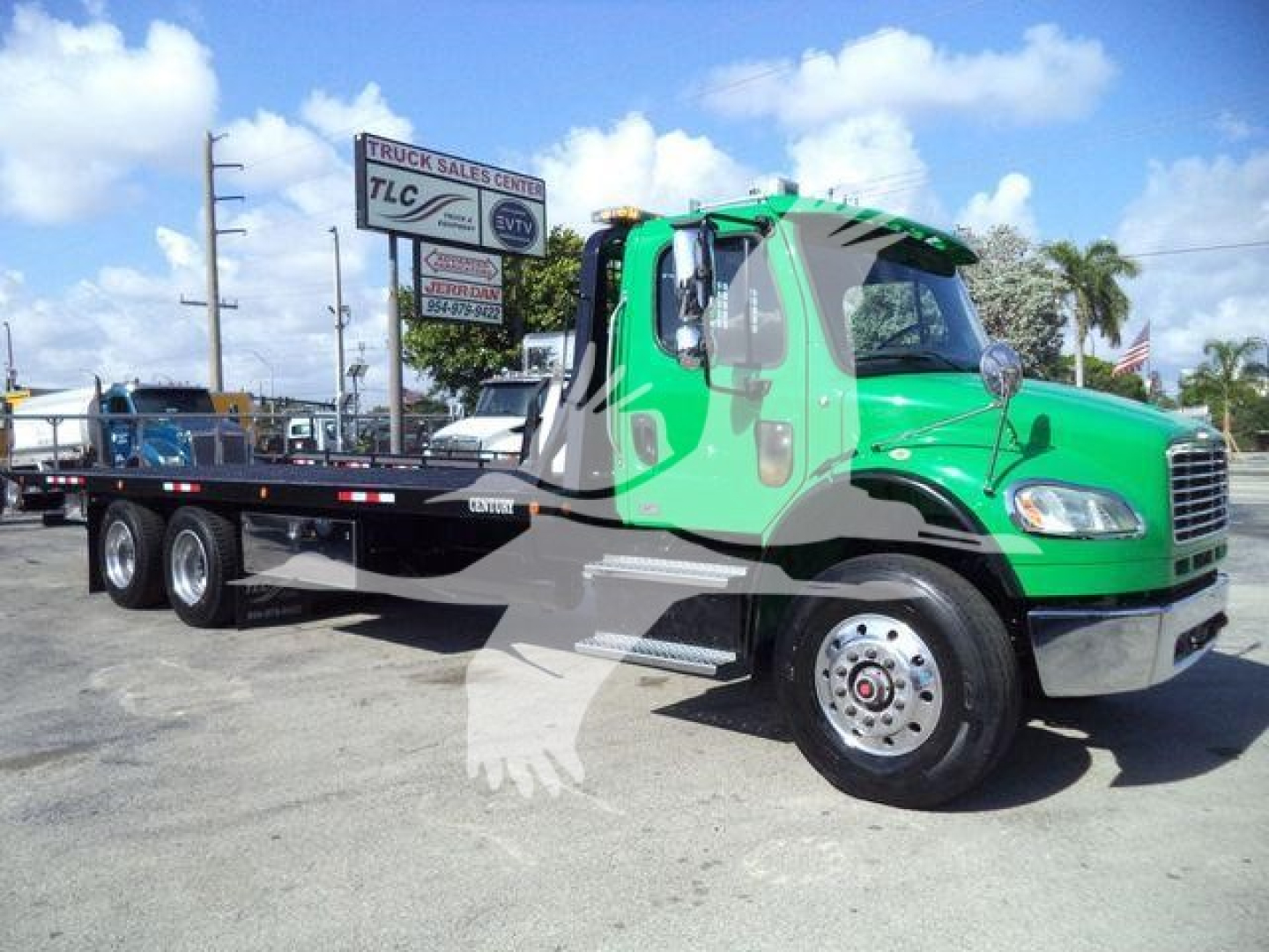 Side view of a green Freightliner M2 106 rollback truck showing flatbed with triple rear axles and chrome front bumper.