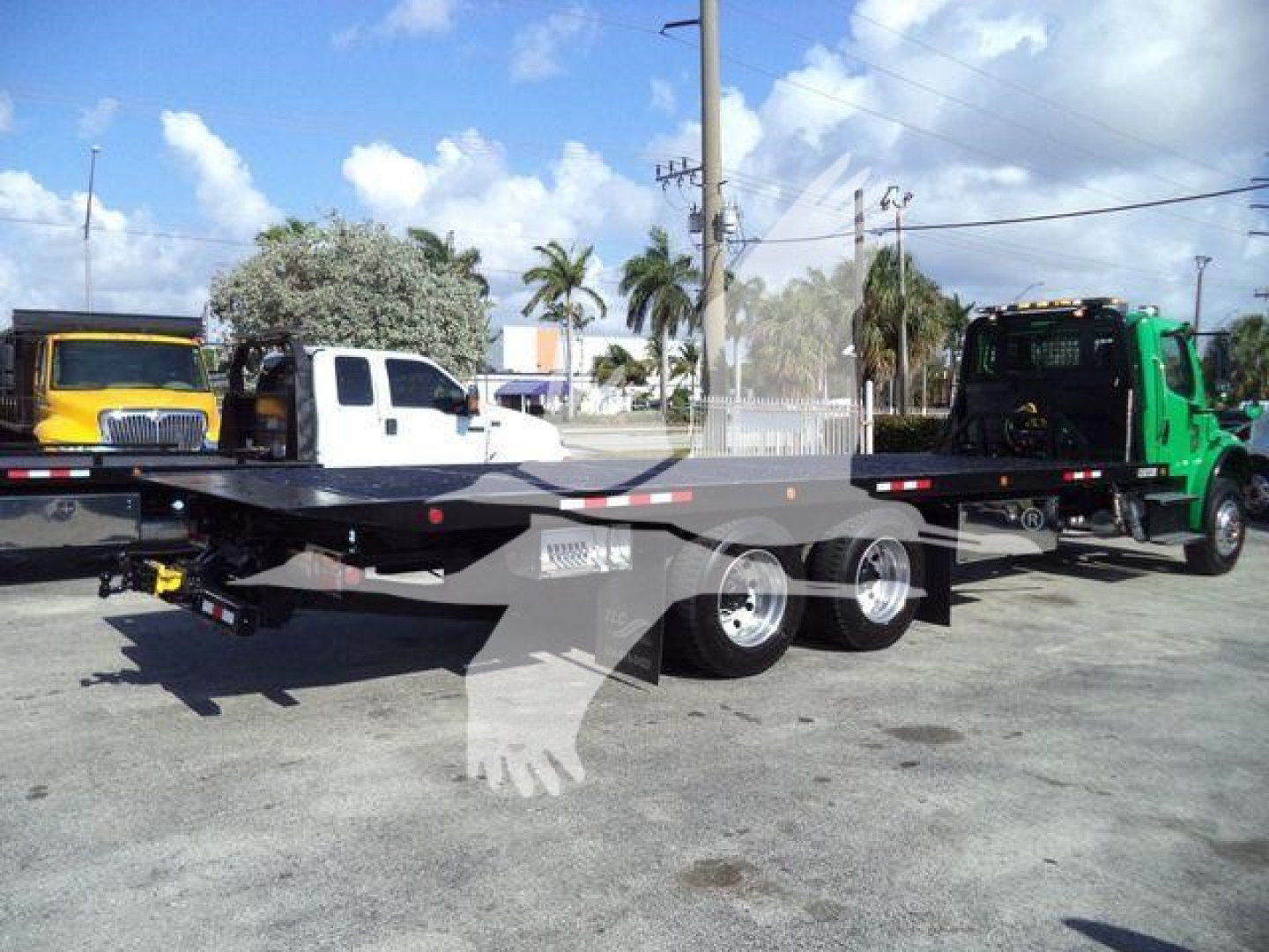 Freightliner M2 106 rollback truck and flatbed trailer in lot with other trucks
