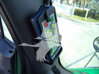 Truck cab interior showing a mounted control panel with green and grey buttons attached near the windshield; window and side mirror visible.