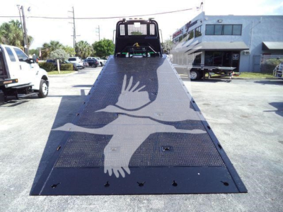 Truck flatbed ramp with a white bird emblem; rear view shows loading deck and black mesh, Freightliner M2 106 rollback vehicle in background.