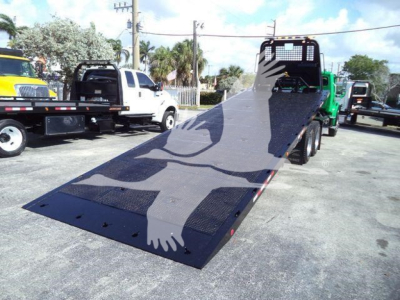 Flatbed ramp of a Freightliner M2 106 rollback truck with a metal loading ramp extended, showing a grated surface and wheel wells in background.